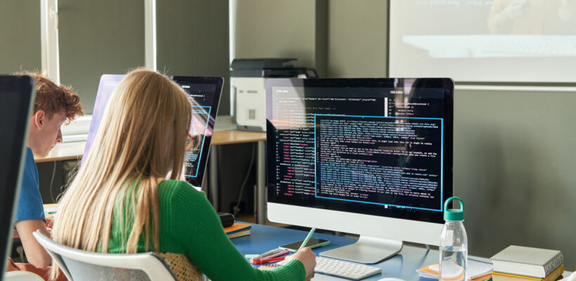 Back view o female student studying on computer during IT class in school or college classroom, copy space